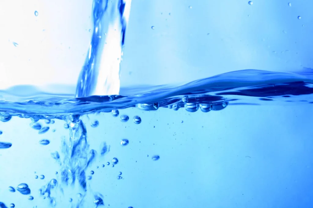 Das Bild zeigt einen dynamischen und visuell beeindruckenden Moment, in dem Wasser gegossen wird und dabei Spritzer und Blasen entstehen. Die Szene betont die Klarheit und Bewegung des Wassers und zeigt die Viskosität und Bewegung der Flüssigkeit.