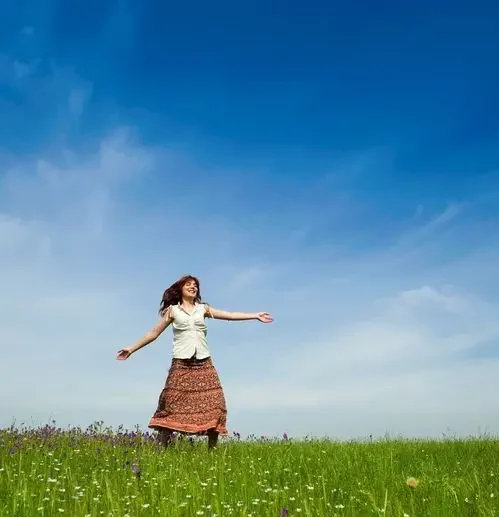 Das Bild zeigt eine Person, die inmitten einer blühenden Blumenwiese steht. Der Himmel ist klar mit nur wenigen Wolken. Das Bild vermittelt das Gefühl von Freude, Freiheit und Verbundenheit mit der Natur, während die Person die Weite des Feldes und den klaren Himmel geniesst.