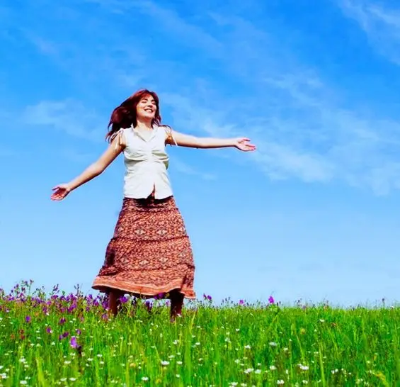Das Bild zeigt eine Person, die inmitten einer blühenden Blumenwiese steht. Der Himmel ist klar mit nur wenigen Wolken. Das Bild vermittelt das Gefühl von Freude, Freiheit und Verbundenheit mit der Natur, während die Person die Weite des Feldes und den klaren Himmel geniesst.